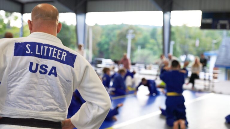 Coach in a USA gi watching a class under the pavilion